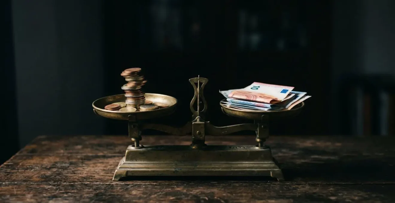 Balance ancienne en laiton avec des pièces empilées d'un côté et des billets pliés de l'autre, symbolisant l'arbitrage entre mensualités réduites et coût total du crédit